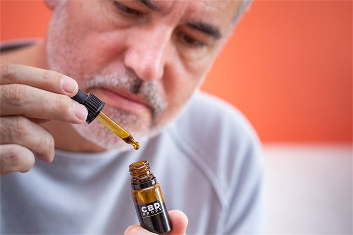 A man holding the dropper of a bottle labeled CBD DROPS