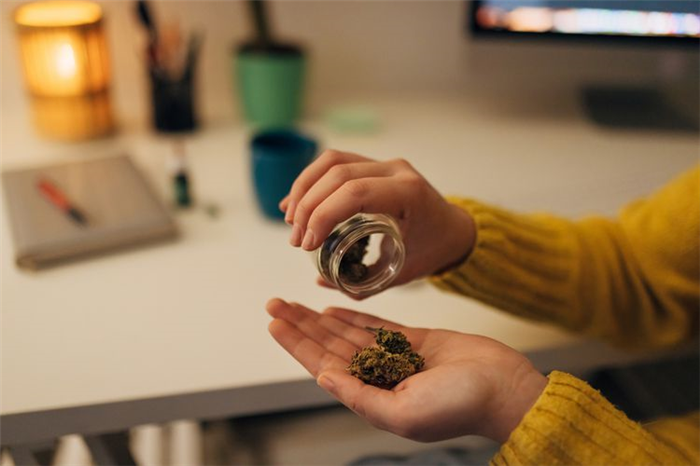 A close-up of the hands of an unrecognizable woman pouring cannabis buds from a jar into her hand