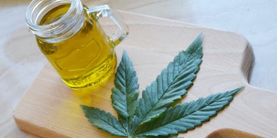 A jar of cannabis oil on a cutting board next to a pot leaf.