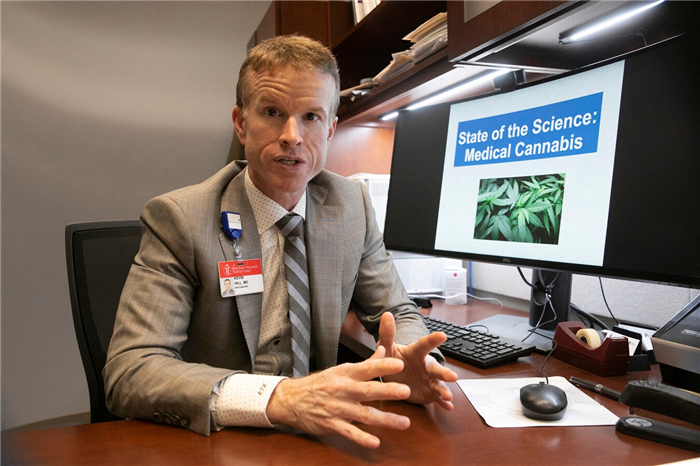 Professor sitting at desk with computer monitor showing marijuana.